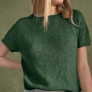 May include: A short-sleeved, forest green knit top. The crew neck shirt has a simple, classic design. The fabric appears soft and comfortable, with a subtle ribbed texture. The sleeves are short and end just above the elbow.