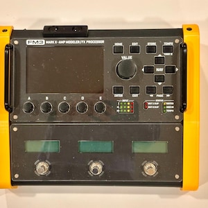 Può includere: Processore di modellazione amplificatore/FX FM3 Mark II nero e giallo. Il dispositivo ha uno schermo, pulsanti e pedali. Il testo "FM3 MARK II - AMP MODELER/FX PROCESSOR" è visibile. Il dispositivo ha una parte superiore e inferiore nere con una cornice gialla.