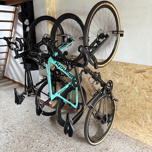 Può includere: Due biciclette montate su un supporto a parete. La bicicletta in primo piano è una bici da corsa Bianchi color turchese brillante con manubrio nero, ruote nere e pneumatici neri. La seconda è una bici da corsa grigia con fianchi beige.