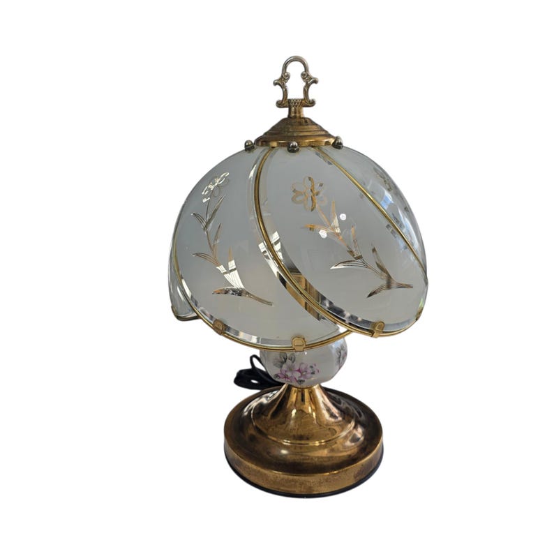 May include: A vintage table lamp with a frosted glass shade featuring floral designs and gold accents. The lamp has a brass base and a decorative finial. The base has a floral design. The lamp is a decorative lighting fixture.