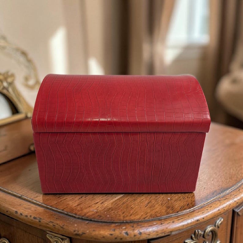 May include: A red, rectangular box with a curved top. The box has a textured, crocodile-like pattern. The box is sitting on a wooden surface with ornate carvings. The box is likely used for storage or decoration.