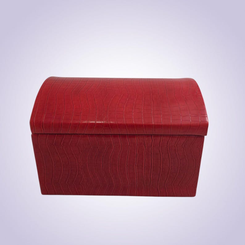 May include: A red, rectangular storage box with a curved top. The box has a textured, crocodile-like pattern. The box is a solid, vibrant red color and appears to be made of leather or a similar material. The box is empty.