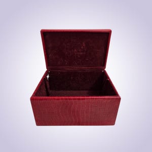 May include: Open red rectangular box with a textured, crocodile-like pattern. The interior is lined with a darker red velvet material. The lid is open, revealing the inside of the box.