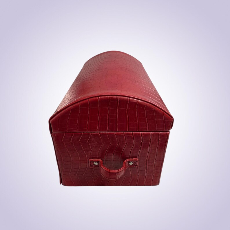 May include: A red, faux-leather chest with a textured, crocodile-like pattern. The chest has a rounded top and a handle on the front. The chest is a decorative storage container.