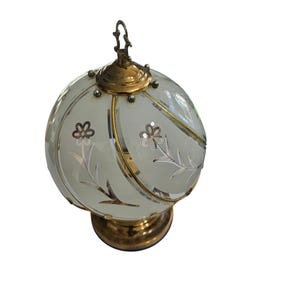 May include: A vintage-style table lamp with a frosted glass globe shade. The shade features etched floral designs and is accented with gold-toned metal trim. The lamp has a brass base and a decorative top.