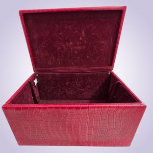 May include: Open red box with a textured, crocodile-like exterior. The interior is lined with a deep red velvet material. The box has a hinged lid, revealing the velvet-lined interior.