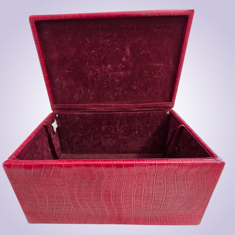May include: Open red box with a textured, crocodile-like exterior. The interior is lined with a deep red velvet material. The box has a hinged lid, revealing the velvet-lined interior.