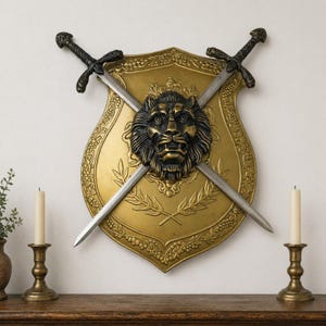 May include: A gold-colored shield with a lion's head in the center, crossed by two swords. The shield has decorative floral and leaf patterns. The swords have black handles. Two candle holders with candles are on the wooden surface below.
