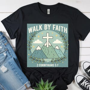 May include: Black t-shirt with a graphic design featuring a white cross, mountains, and the text "WALK BY FAITH" and "2 CORINTHIANS 5:7". The design is surrounded by a green wreath. The shirt is paired with blue jeans and black trainers.