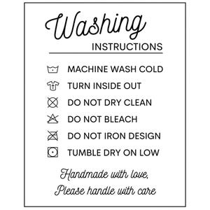 May include: A rectangular white sign with black text and icons titled Washing Instructions. It lists: Machine wash cold, Turn inside out, Do not dry clean, Do not bleach, Do not iron design, Tumble dry on low. It ends with Handmade with love, Please handle with care.