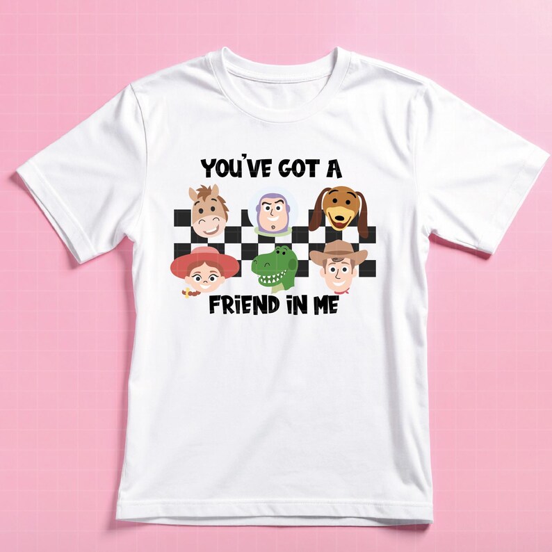May include: A white short-sleeve t-shirt featuring a black and white checkered pattern with cartoon character faces including a horse, space ranger, dog, cowgirl, dinosaur, and cowboy. The text reads YOU'VE GOT A FRIEND IN ME in black letters.