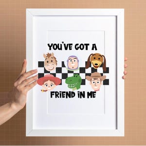 May include: A white framed print featuring a black and white checkered pattern with cartoon character faces including a horse, space ranger, dog, cowgirl, dinosaur, and cowboy. The text reads YOU'VE GOT A FRIEND IN ME in bold black letters.