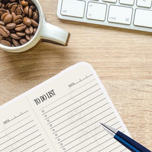 May include: A cream-coloured paper notepad featuring four distinct sections labelled TO DO LIST with horizontal lines and circular checkboxes for tasks. A blue and silver ballpoint pen rests diagonally across the notepad pages.