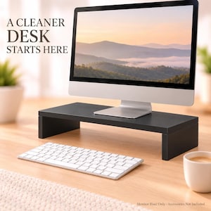 May include: A black rectangular monitor riser stand with a flat top and two side supports. The text A CLEANER DESK STARTS HERE is visible on the left. The stand supports a computer monitor, with a white keyboard placed in front of the riser.