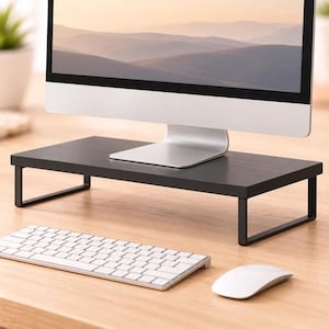 May include: A black rectangular monitor stand featuring a flat top surface and two sturdy metal legs. The stand is designed to elevate a computer screen, providing a stable base for desktop equipment while maintaining a clean and functional appearance.
