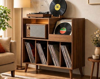 May include: A mid-century modern record player cabinet in a warm wood finish. It features a turntable, speaker, and storage for vinyl records. A black vinyl record is displayed on top, with other records stored inside the cabinet.