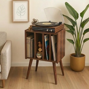 Puede incluir: Mueble tocadiscos de madera oscura con tocadiscos incorporado. El mueble tiene espacio para discos de vinilo y libros. Una impresión botánica enmarcada cuelga de la pared. Altura aproximada: 75 cm.