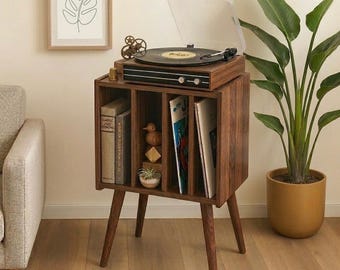 May include: A mid-century modern record player stand in dark wood. The stand features a built-in record player on top and storage for vinyl records and books below. A framed botanical print hangs on the wall.