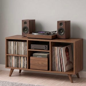 May include: A wooden media unit with a record player, speakers, and storage for vinyl records and CDs. The unit has a mid-century modern design with angled legs and a warm brown finish. The speakers are a matching brown colour.