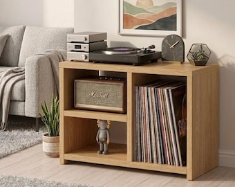 May include: A light oak wood media console with a turntable, stereo components, and a speaker. The console has two shelves, one with vinyl records and the other with a speaker. A framed landscape art piece hangs above the console.