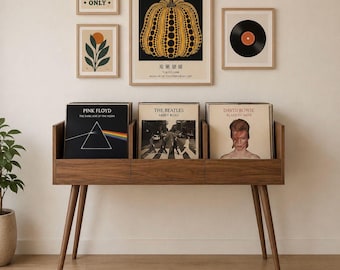 May include: A wooden record storage unit with angled legs holds three vinyl record albums. Above, framed art includes a Yayoi Kusama pumpkin print, a record, and two other prints. The text "GOOD VIBES ONLY" is visible.