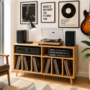 May include: A wooden record player console with a turntable, speakers, and a receiver. The console holds vinyl records and is decorated with framed art and a guitar. A black lamp sits on the console.