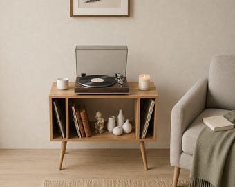 May include: A wooden record player stand with a built-in record player, holding a vinyl record. The stand has open compartments for storage, with books and decorative items. A lit candle and a white mug sit on the stand.