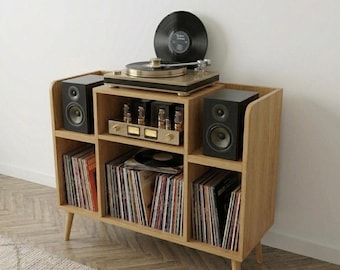 May include: A wooden record player console with a turntable, speakers, and storage for vinyl records. The console has a light wood finish and a mid-century modern design. A black vinyl record is on the turntable.