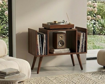 May include: A mid-century modern record player stand in dark wood. The stand features a turntable, speaker, and storage for vinyl records. The stand has angled legs and is placed in a well-lit room with a neutral color palette.