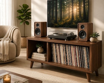 May include: A walnut-toned media console with a built-in record player, speakers, and a collection of vinyl records. The console has a mid-century modern design, with angled legs and open shelving. A flat-screen TV is mounted above the console.