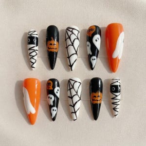May include: A set of ten almond-shaped press-on nails featuring Halloween designs. Patterns include black and white mummy wraps, orange pumpkins on black, black spiderwebs on white, white ghosts on black, and solid orange with white ghost accents.