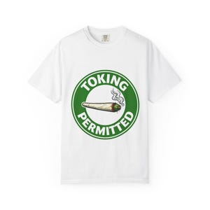 May include: White t-shirt featuring a green circular design with the words "TOKING PERMITTED." The graphic includes a lit joint with smoke. The t-shirt has a crew neck and is made of a soft material.