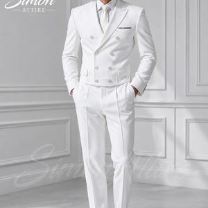 May include: A white double-breasted suit featuring a cropped jacket with a belted waist, peak lapels, and silver-toned buttons. The ensemble includes a matching white dress shirt, a white necktie, and white dress shoes. The Simon Attire logo is visible.