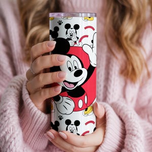May include: A white and red tumbler featuring Mickey Mouse. The tumbler has a repeating pattern of Mickey Mouse and his iconic gloves. The tumbler is cylindrical and appears to be made of stainless steel.