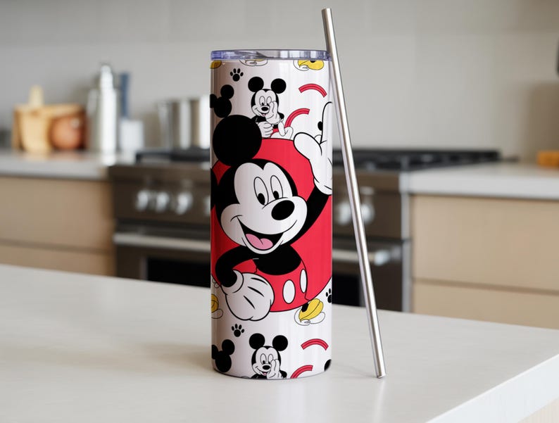 May include: A white tumbler featuring Mickey Mouse in a red outfit, with a stainless steel straw. The tumbler has a repeating pattern of Mickey Mouse, paw prints, and yellow accents. The tumbler is cylindrical.