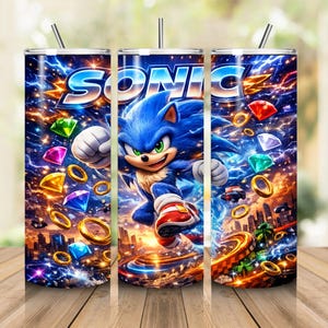 May include: A cylindrical tumbler featuring a vibrant graphic of Sonic the Hedgehog in a dynamic running pose. The design includes the word SONIC, golden rings, and colorful gemstones set against a background of blue lightning and a city landscape.