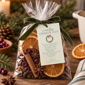 May include: A clear plastic bag filled with dried orange slices, cinnamon sticks, star anise, and cranberries. A green velvet ribbon ties the top, and a tag reads: winter SIMMER POT, POUR CONTENTS INTO BOILING WATER AND REDUCE TO SIMMER. REPLENISH WATER AS NEEDED. ENJOY! Olivia's HOMEMADE GOODS.
