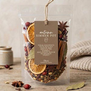 Può includere: Un sacchetto di plastica trasparente riempito con fette di arancia essiccate, bastoncini di cannella, anice stellato e bacche. Un'etichetta rettangolare marrone è legata con uno spago, riportante il testo "autumn SIMMER POT".