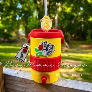 May include: A yellow and red insulated tumbler with a straw and decorative charms. The tumbler features the text "Tale as old as time" and a rose graphic. A charm of a rose in a bell jar is attached.