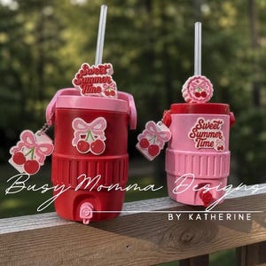 May include: Two insulated tumblers, one red and one pink, with cherry decorations. Each has a straw and a cherry charm. The text "Sweet Summer Time" is on the top of each tumbler. Ideal for summer drinks.