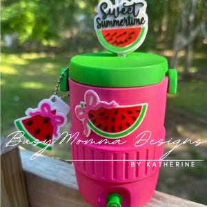 May include: A pink and green water cooler with a watermelon theme. The cooler has a green lid and a watermelon slice design. The text "Sweet Summertime" is on the straw topper. The text "Busy Momma Designs by Katherine" is on the cooler.