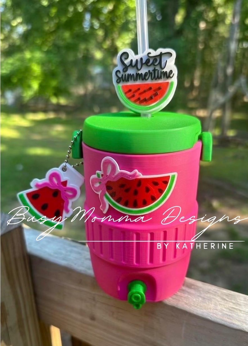 May include: A pink and green water cooler with a watermelon theme. The cooler has a green lid and a watermelon slice design. The text "Sweet Summertime" is on the straw topper. The text "Busy Momma Designs by Katherine" is on the cooler.
