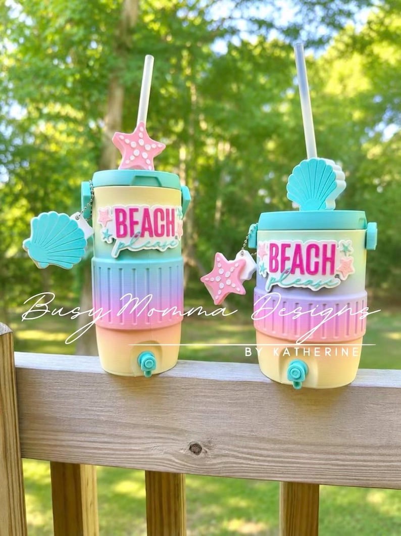 May include: Two beach-themed water coolers with a light blue lid, yellow base, and pastel rainbow centre. Each cooler has a straw, a starfish and seashell charm, and the words "Beach Please". The coolers are ideal for keeping drinks cool.