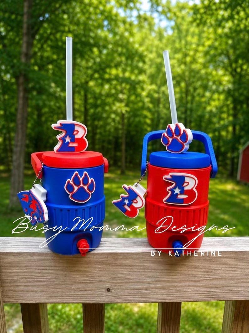 May include: Two red and blue insulated water coolers with straws. Each cooler has a matching lid, handle, and decorative charm. One has a paw print and the other has a letter "B" design. The text "Busy Momma Designs" and "By Katherine" are visible.