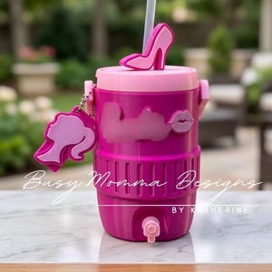 May include: A pink and fuchsia water cooler with a high-heeled shoe accent on the lid. The cooler has a straw, a charm with a silhouette, and the text "Busy Momma Designs BY KATHERINE".