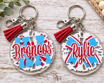 Peut inclure: Deux porte-clés circulaires en acrylique avec le texte en écriture pailletée rouge Broncos et Rylie. Chaque porte-clés comprend un anneau en métal argenté, un fermoir mousqueton et un pompon en similicuir rouge avec des accents blancs et bleu clair.