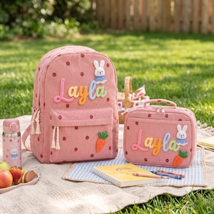 Puede incluir: Una mochila y una bolsa de almuerzo a juego de pana rosa con estampado de fresas, un parche de conejo blanco, un parche de zanahoria naranja y el nombre Layla en letras 3D de colores. Se incluye una botella de agua rosa a juego con un conejo.
