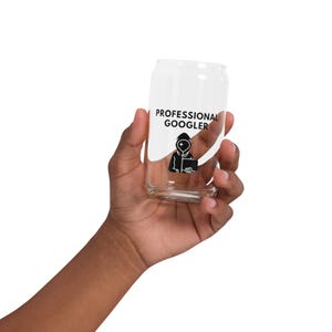 Puede incluir: Un vaso transparente con forma de lata que presenta el texto negro PROFESSIONAL GOOGLER y un gráfico negro de una figura con capucha sosteniendo una tableta. El diseño incluye una forma de acento curva blanca detrás del texto y el gráfico.