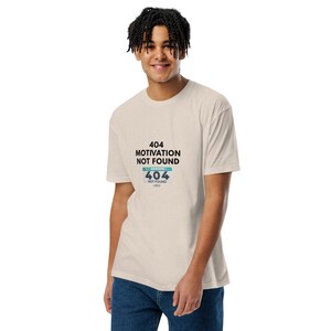 Pode incluir: Uma t-shirt de manga curta bege com o texto preto 404 MOTIVATION NOT FOUND acima de um gráfico de uma janela de erro do navegador que também exibe o texto 404 NOT FOUND numa caixa retangular azul clara e branca no peito.
