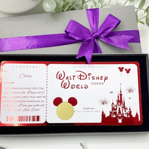 Könnte beinhalten: Eine Geschenkbox mit grauem Deckel und einer lila Schleife. Im Inneren befindet sich eine rot-weiße Karte im Ticketstil für Walt Disney World in Florida. Die Karte trägt den Text "SURPRISE!" und "Chloe".